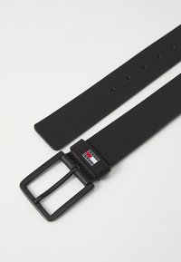Zwarte synthetische riem met een matte rechthoekige gesp, met een merkaccent en meerdere gaatjes voor maatverstelling.
