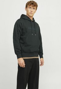 Dark green hoodie made of soft fabric, featuring a front pocket and drawstrings, with "ORIGINALS" printed on the chest and ribbed cuffs.