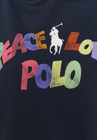 Polo blu navy con stampa grafica che presenta un testo colorato e stilizzato che recita "PACE AMORE POLO" e un silhouette di un cavaliere di polo bianca.
