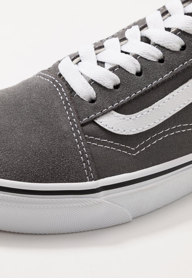 Baskets en toile grises avec des lacets et des coutures blanches, présentant une bande latérale blanche et une semelle en caoutchouc texturée avec un accent noir.