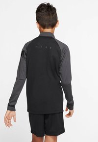 Svart långärmad träningströja med grå detaljer, rund krage och "NIKE"-logotyp på baksidan, matchad med svarta shorts.