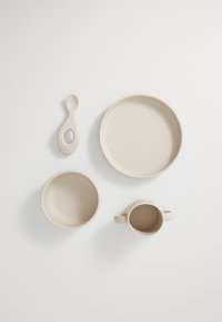 Beige ceramic tableware set includes a shallow plate, bowl, cup with handle, and spoon, featuring smooth textures and rounded shapes.