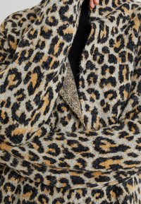 Płaszcz w wzór lamparta w odcieniach szarości, czerni i brązu, z miękką teksturą, długimi rękawami i kołnierzem typu szal.