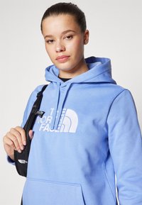 Felpa blu chiaro con tasca frontale, caratterizzata da una stampa bianca del logo. Materiale in cotone con una texture morbida e cappuccio regolabile con cordino.