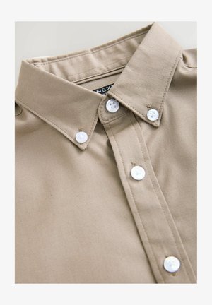 Beige skjorta med krage och en strukturerad design, som har vita knappar och en mjuk bomullstextur. Etiketten säger "NEXT."