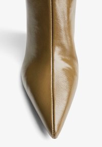 Boots din piele sintetică maro, cu vârf ascuțit, finisaj lucios și detalii vizibile cu cusături, evidențiind un design elegant și aerodinamic.