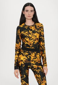 Top a maniche lunghe e leggings coordinati in un tessuto nero con intricati motivi barocchi dorati, caratterizzati da un colletto rotondo e uno stile aderente.