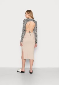 Langärmliges Oberteil mit einem schwarz-weißen Polka-Dot-Muster, offenem Rücken, kombiniert mit einem beigen, gerippten Midikleid, das einen Seitenschlitz aufweist.