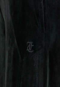 Melna kordūra auduma ar mīkstu tekstūru, kurā ir izšūta melna burts "F". Vienkāršs dizains ar maigu spīdumu.