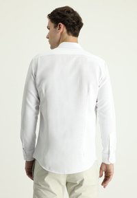 Camicia bianca a maniche lunghe con tessuto strutturato, orlo curvato e polsini con bottone. Presenta un colletto classico e una spalla posteriore per maggiore struttura.