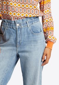 Jeans de mezclilla de color azul claro con cinturilla elástica, bolsillos frontales y un ajuste de altura media. Textura suave con un sutil efecto de lavado.