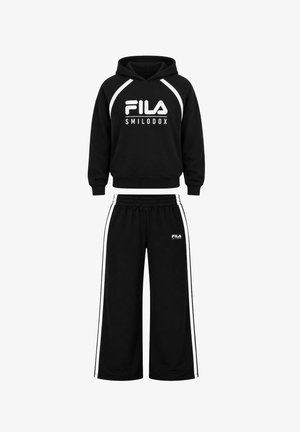 Zwei junge Erwachsene, die passende schwarze FILA-Hoodies und Hosen mit weißen Sneakern tragen, stehen nebeneinander vor einem weißen Hintergrund.