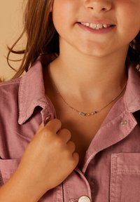 Goldfarbener Kettenanhänger mit mehrfarbigen dekorativen Perlen in verschiedenen Formen; getragen mit einem rosa Kragenhemd.