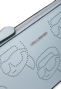 Ljusblå läderplånbok med perforerat mönster och silverfärgad hårdvara, med dragkedjestängning och präglad logotypdetalj.