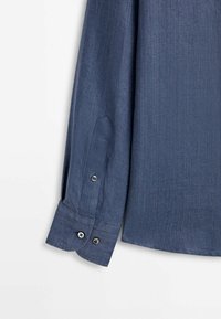 Manche de chemise bleu à manches longues avec poignet à double bouton et fente de manche à bouton unique sur fond blanc.