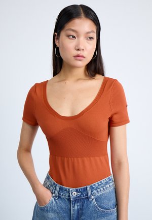 Rostfarget tettsittende topp med kortermet, dyp V-hals og ribbet tekstur. Kombinert med høyhårede denimshorts med en falmet finish.