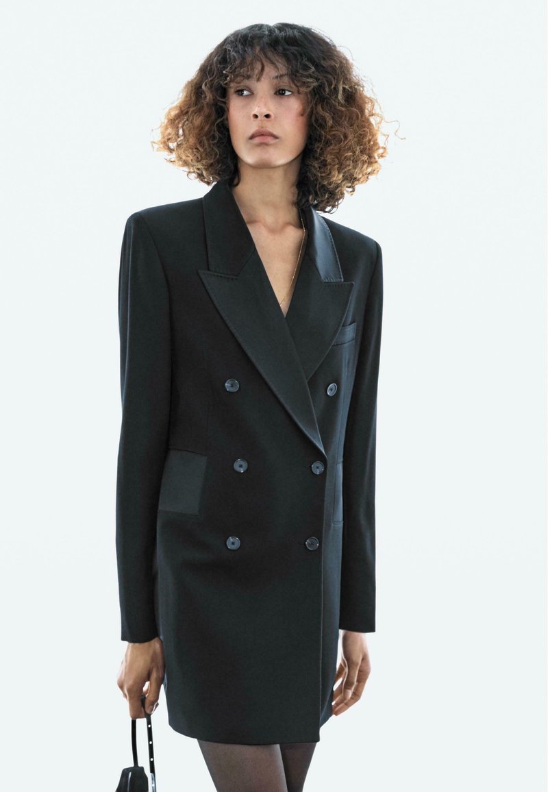 Schwarzes, doppelt geknöpftes Blazer-Kleid mit breiten Revers, zwei vorderen Taschen und Knopfakzenten, gefertigt aus glattem Stoff.
