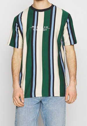 Mężczyzna ubrany w krótki rękaw t-shirt z okrągłym dekoltem w pionowe paski w kolorach zielonym, beżowym, niebieskim i czarnym oraz białym napisem, w połączeniu z jasnoniebieskimi dżinsami.