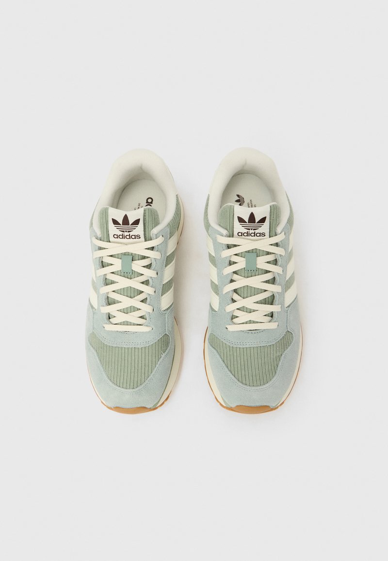 Paire de baskets Adidas vert clair avec lacets et bandes crème, vues de dessus sur fond blanc.