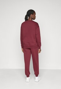 Bordeaux sweatshirt og matchende joggers lavet af blødt stof, med ribbede manchetter og kant, i en afslappet pasform uden synlige logoer eller mønstre.