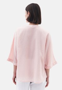 Blusa a righe rosa chiaro con vestibilità ampia, maniche larghe e una texture sottile. La vista posteriore mostra un semplice colletto tondo e spalle scese.