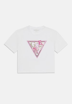 Camiseta blanca recortada con un diseño de logo triangular con lentejuelas plateadas, rosas y doradas que forman la palabra "GUESS" en el centro.