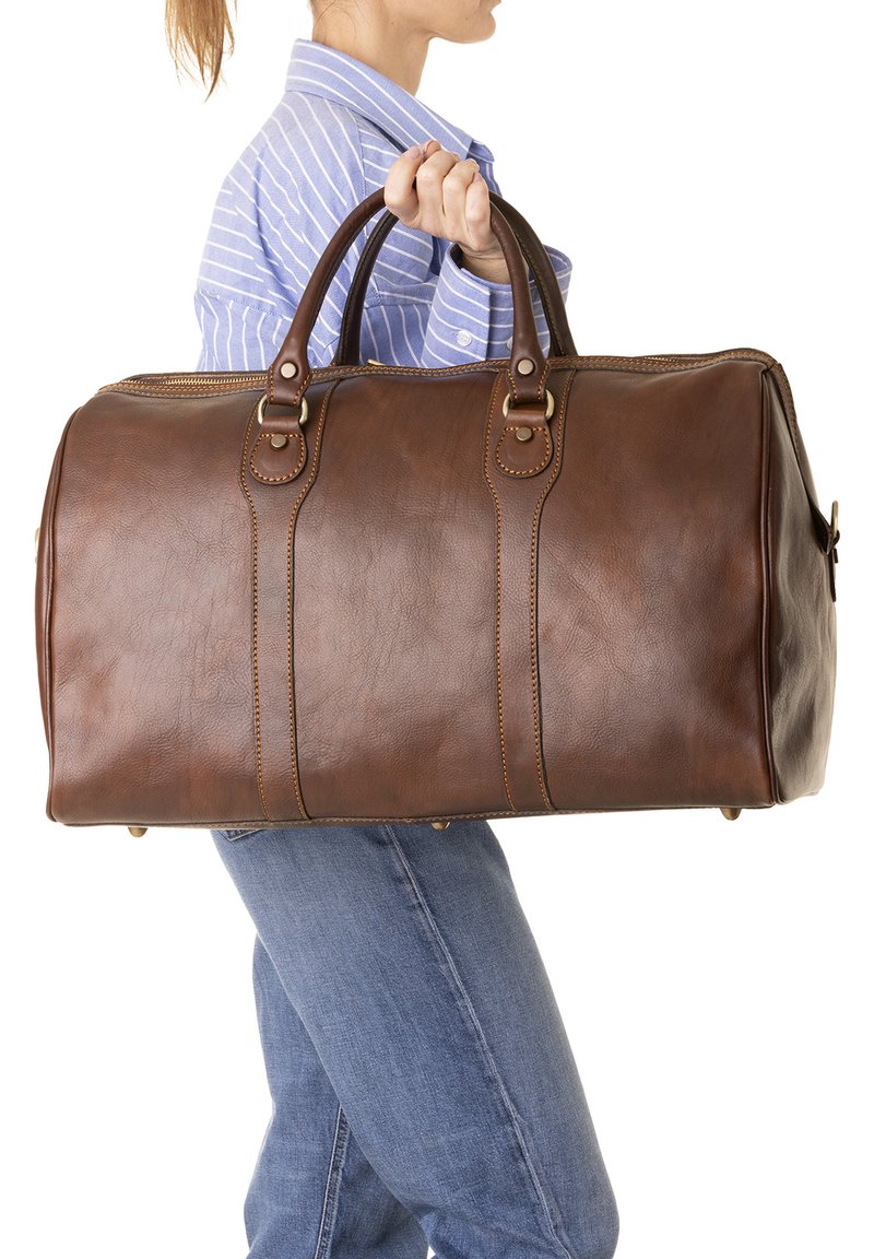 Sac de sport en cuir marron avec des poignées doubles, des coutures contrastées et une forme arrondie. Surface texturée avec de petits pieds en métal pour la stabilité.