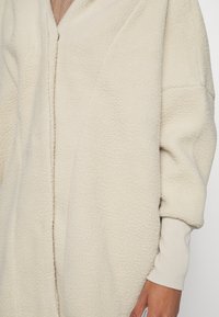 Krämfärgad oversized fleecejacka med en texturerad yta, djup V-ringning och ribbade muddar, med en dragkedja fram.