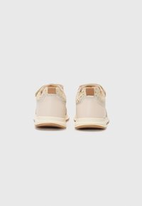 Des baskets beiges avec un arrière texturé, présentant un accent à motif jaune sur le talon et une semelle de couleur claire.
