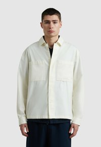 Lichtcrème oversized shirt met twee borstzakken, knoopsluiting en lange mouwen. Gemaakt van een soepele stof met een subtiele textuur.