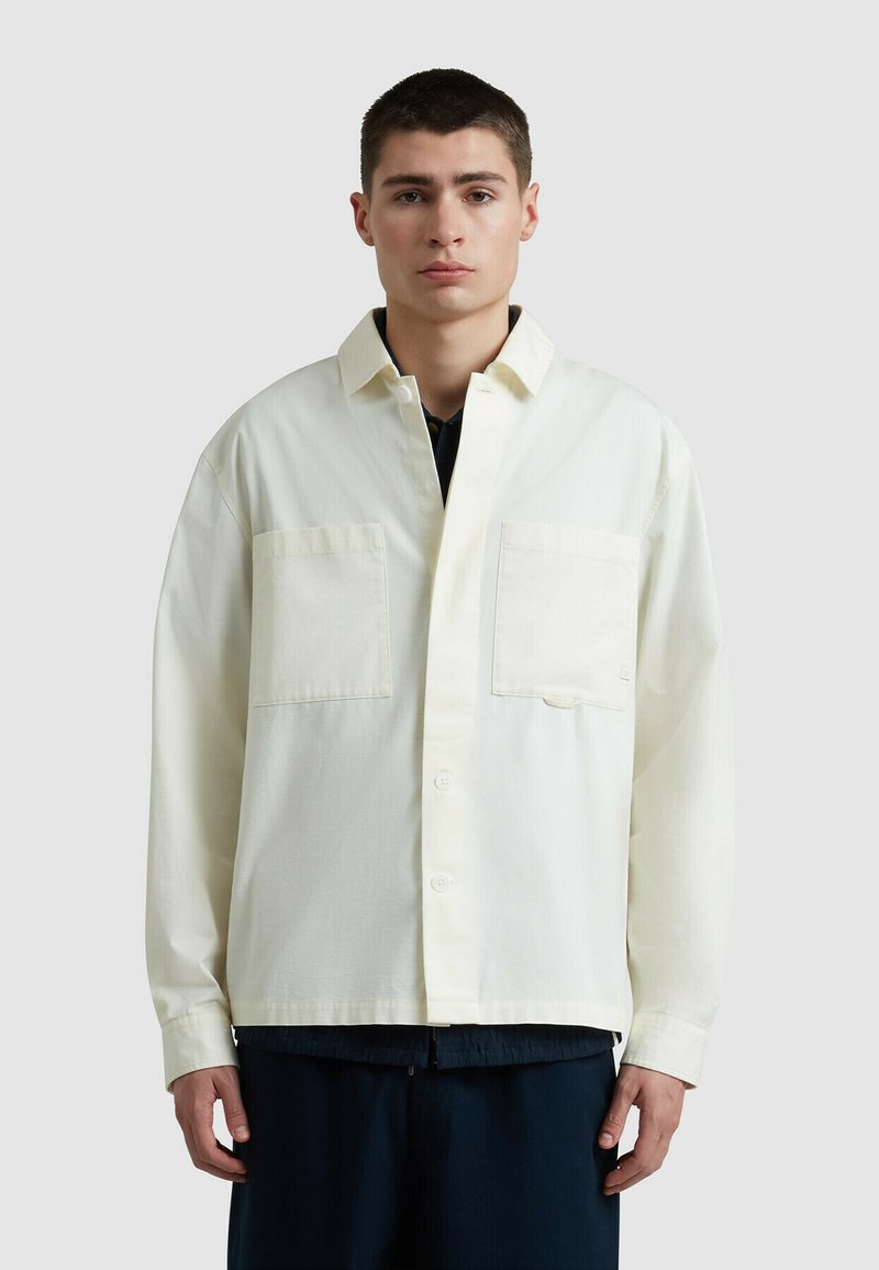 Lichtcrème oversized shirt met twee borstzakken, knoopsluiting en lange mouwen. Gemaakt van een soepele stof met een subtiele textuur.