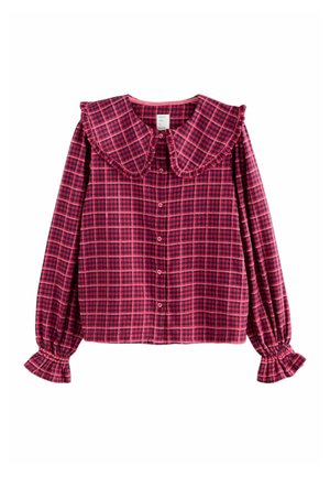 Punainen ja laivastonsininen ruudullinen paita, jossa on suuri, röyhelömäinen kaulus, napitus ja pleiattu hiha. Valmistettu pehmeästä kankaasta.