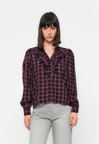 Dark plaid blouse with ruffled neckline and front buttons. Features long sleeves with gathered cuffs. Main colors: navy, red, and white.