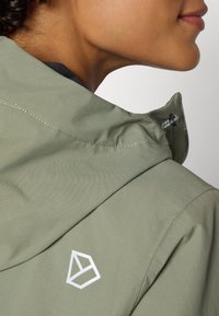 Light green outdoor jacket with a high collar, featuring a white geometric logo on the shoulder and visible seam detailing.