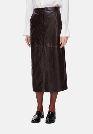 Gonna midi in pelle marrone con una texture liscia, caratterizzata da una chiusura frontale con bottoni e cuciture verticali. Modello che indossa mocassini neri.