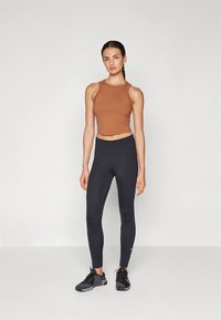 Brązowy krótki top typu tank w połączeniu z czarnymi legginsami z wysokim stanem. Strój ma dopasowany krój i wykonany jest z elastycznej tkaniny.