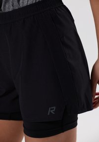 Pantalones cortos deportivos negros con cinturilla elástica y paneles laterales de malla. Presenta un logo reflectante y un diseño ajustado para mayor comodidad y libertad de movimiento.