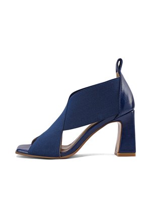 Sandalo con tacco alto a punta aperta di colore blu navy con ampie fasce elastiche che attraversano il piede e un robusto tacco a blocco.