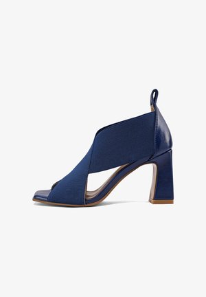 Sandalo con tacco alto a punta aperta di colore blu navy con ampie fasce elastiche che attraversano il piede e un robusto tacco a blocco.