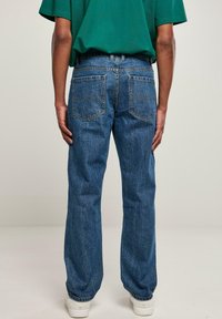 Vaqueros de mezclilla azul claro con un corte relajado, que incluyen bolsillos traseros y un diseño de pierna recta, combinados con una camiseta verde de gran tamaño.