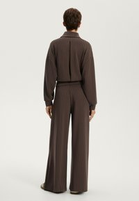 Bruine uitgelijnde gecoördineerde outfit met een losse, hoge col top en wijde broekspijpen. Zacht materiaal met uitgesproken verticale strepen.