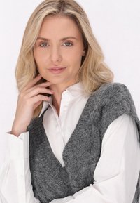 Grå strikket vest over en hvid skjorte med krave og knapper, der har et struktureret stof med brede armhuller og V-hals design.