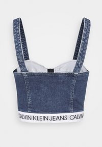 Džínový cropped top s nastavitelnými ramínky, se strukturovaným designem a bílou elastickou páskou s logem "CALVIN KLEIN JEANS" na lemu.