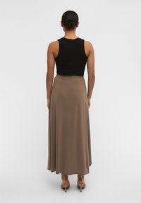 Un débardeur noir à côtes associé à une jupe fluide de longueur cheville en taupe, avec une texture lisse et une taille légèrement élastique.