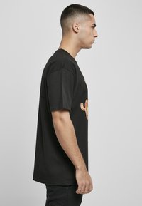 Črna bombažna majica s kratkimi rokavi, ki na sprednji strani prikazuje pisano grafiko kaktusa. Ima okroglo ovratnico in sproščen kroj.