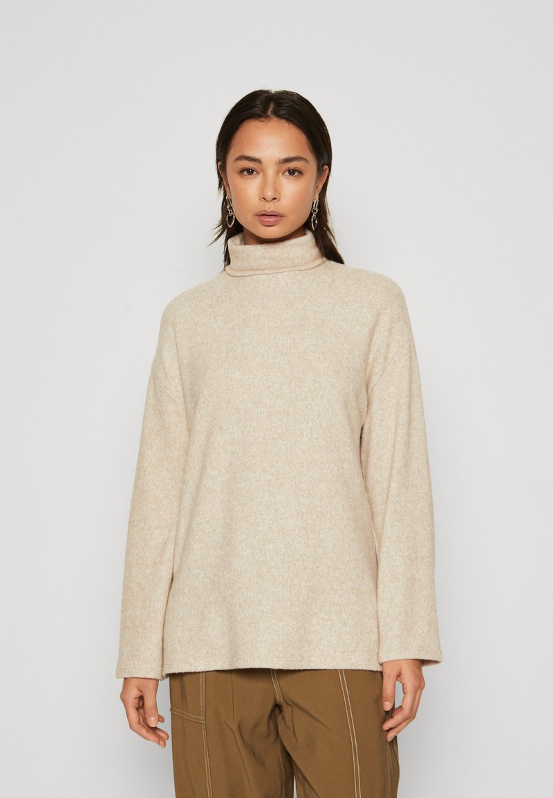 Beige coltrui van een zachte, gestructureerde stof met een ontspannen pasvorm en lange mouwen. Minimalistisch ontwerp, zonder zichtbare patronen of hardware.