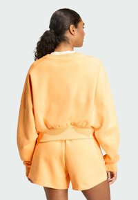 Pomarańczowa bluza z luźnym krojem i ściągaczami, w zestawie z dopasowanymi szortami. Miękka struktura, elastyczny pas i brak widocznych wzorów.
