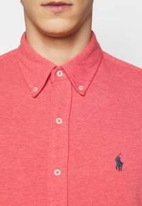 Polo shirt rosso testurizzato con colletto button-down, cinque bottoni e logo a cavallo ricamato in blu navy sul lato sinistro del petto.