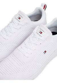 Paire de baskets blanches en maille Tommy Hilfiger avec des lacets blancs et un logo sur la languette et le côté, vues de dessus sur un fond blanc.