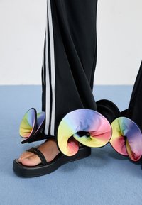 Black platform sandals with two straps, featuring colorful, horn-shaped accents in gradient shades of pink, yellow, and blue.
